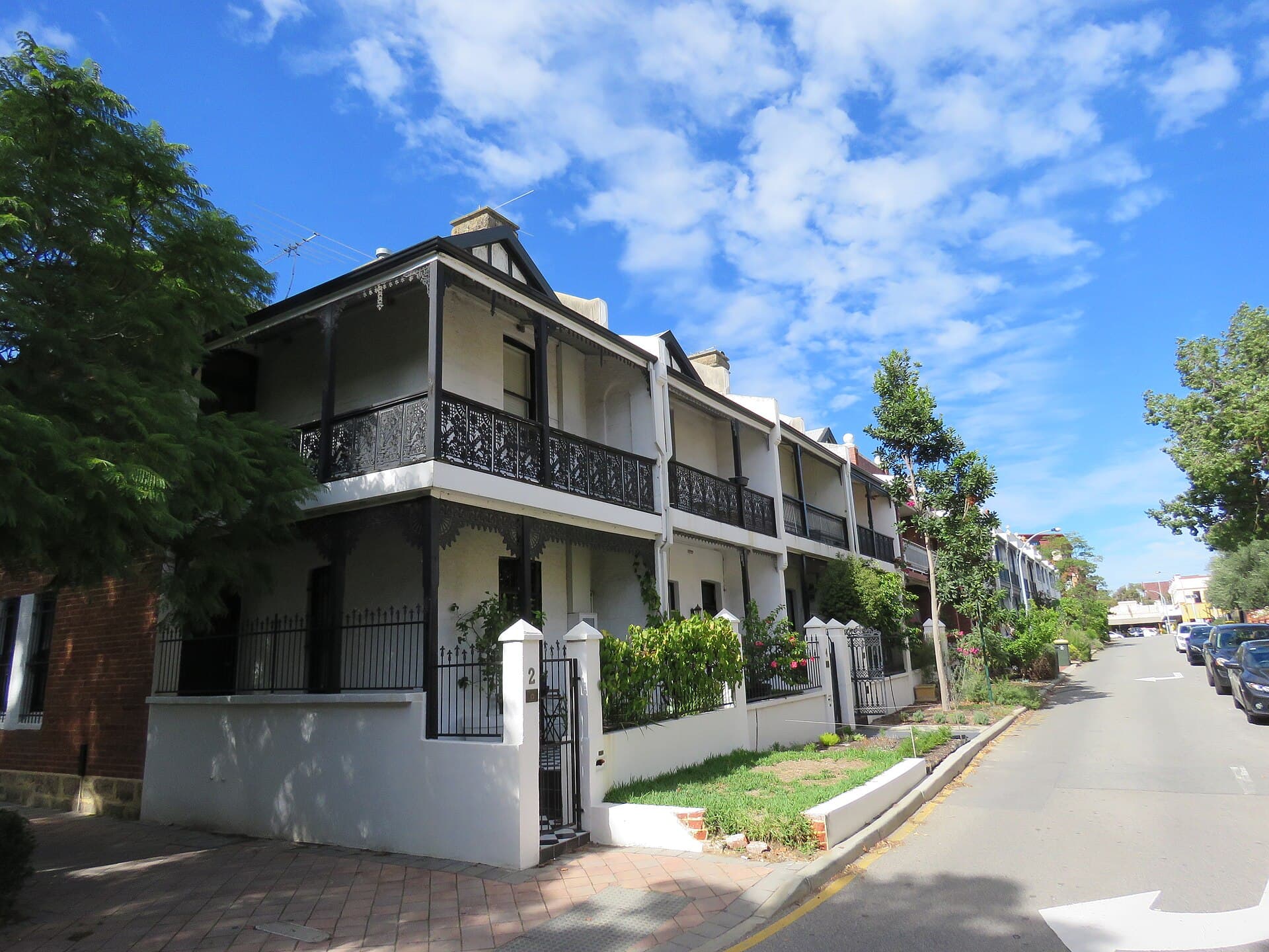 White two-storey terrace row with black iron-lace verandahs, a low fence and a small front garden on a quiet suburban corner