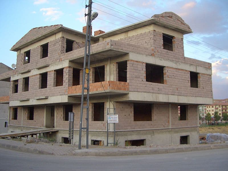 Unfinished two-storey concrete-block house with empty window openings on a suburban corner